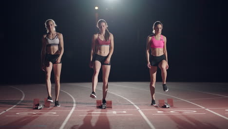 Slow-motion-3-female-runners-running-to-the-camera-in-a-sports-arena.-Track-and-field-athletics-competition-running-in-the-dark.-Race-together